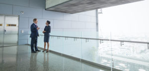 Businessman and businesswoman walking and talking on elevated walkway near modern office architecture and window